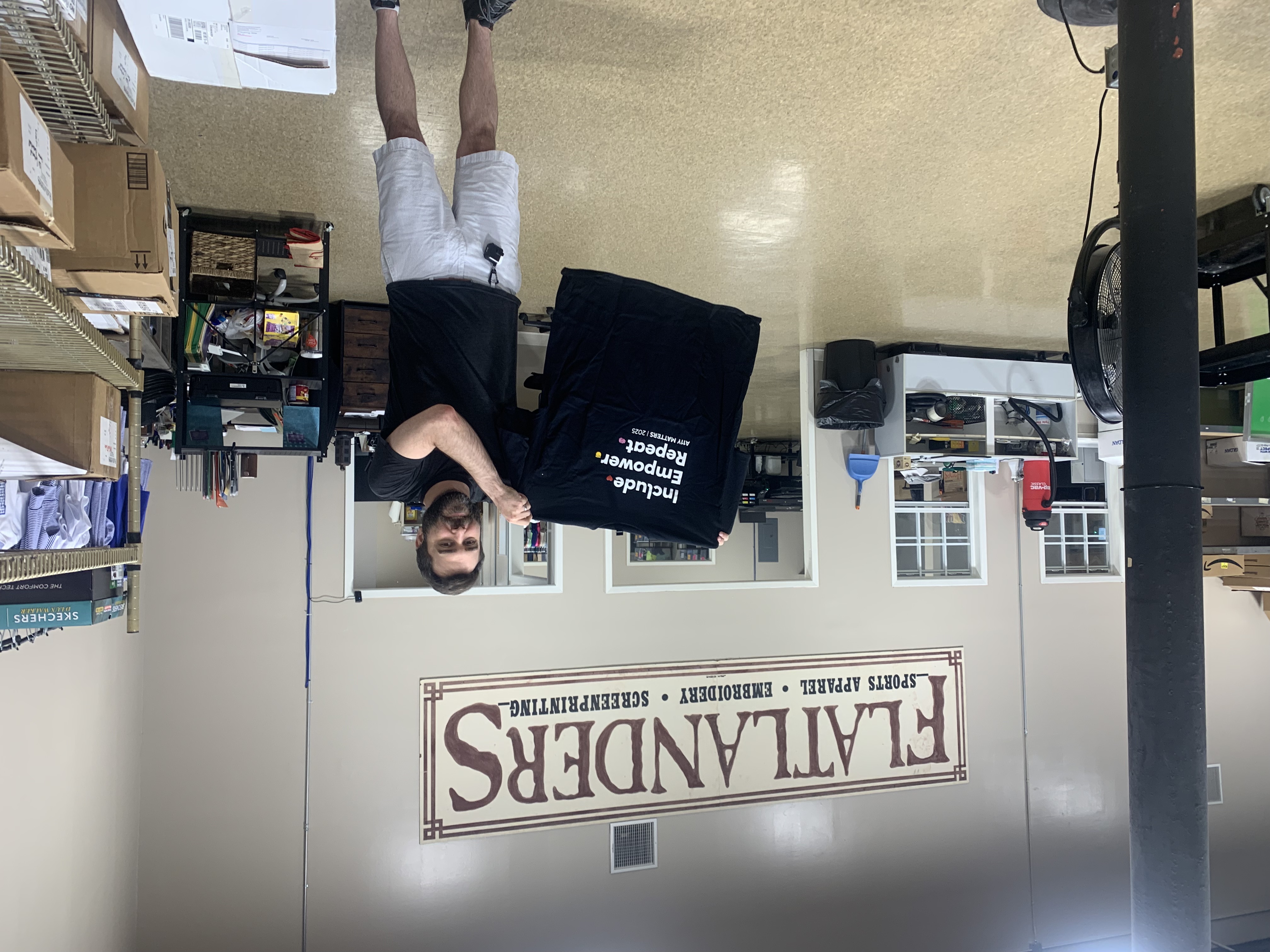 A man holding up the custom printed accessibility shirt that reads: Include, Empower, Repeat